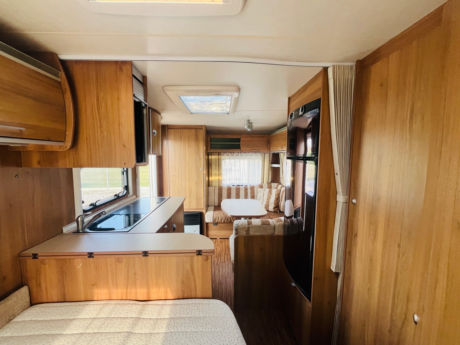 Obrázek interiéru karavanu s dřevěným obložením a pohodlným sezením. Elegantní a prostorný design pro cestování.