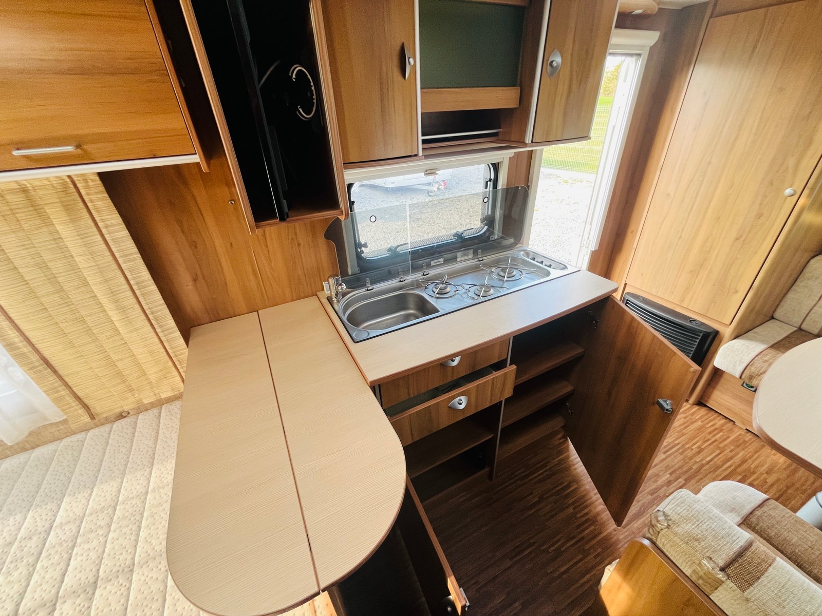 Obrázek interiéru karavanu s kuchyňkou a úložným prostorem. Moderní design s dřevěným dekorem.