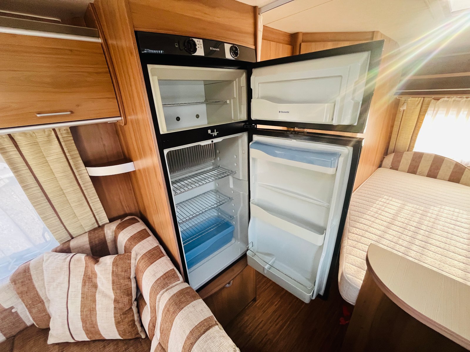 Obrázek interiéru karavanu s moderním chladničkou a pohodlným posezením. Ideální pro cestování a relaxaci.