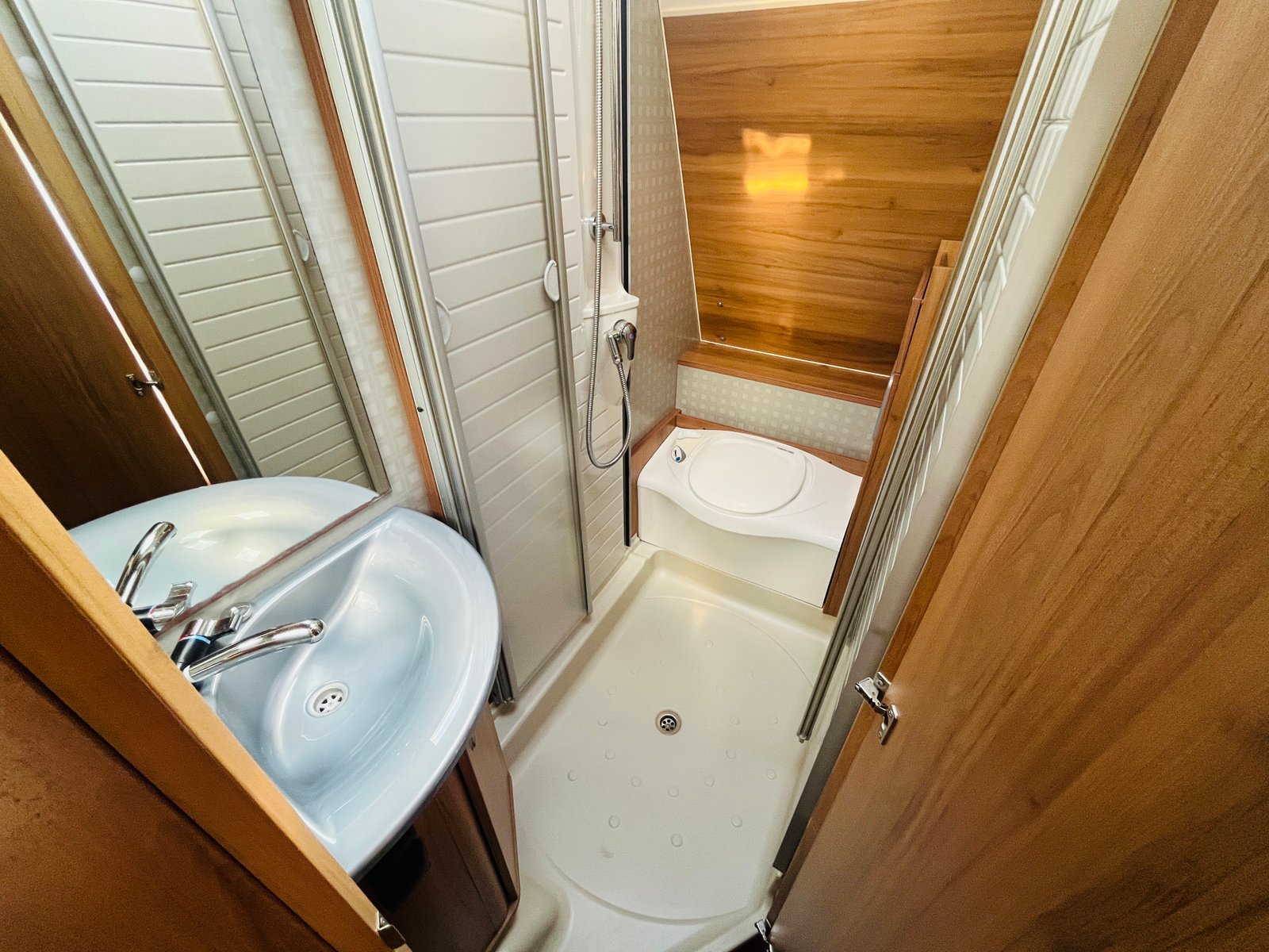 Obrázek interiéru karavanu s koupelnou, umyvadlem, sprchou a toaletou, moderním a prostorným designem.