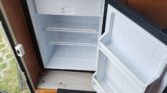 Interiér karavanu Dethleffs s otevřeným ledničkou a dřezem. Moderní design a praktické uspořádání pro pohodlné kempování.