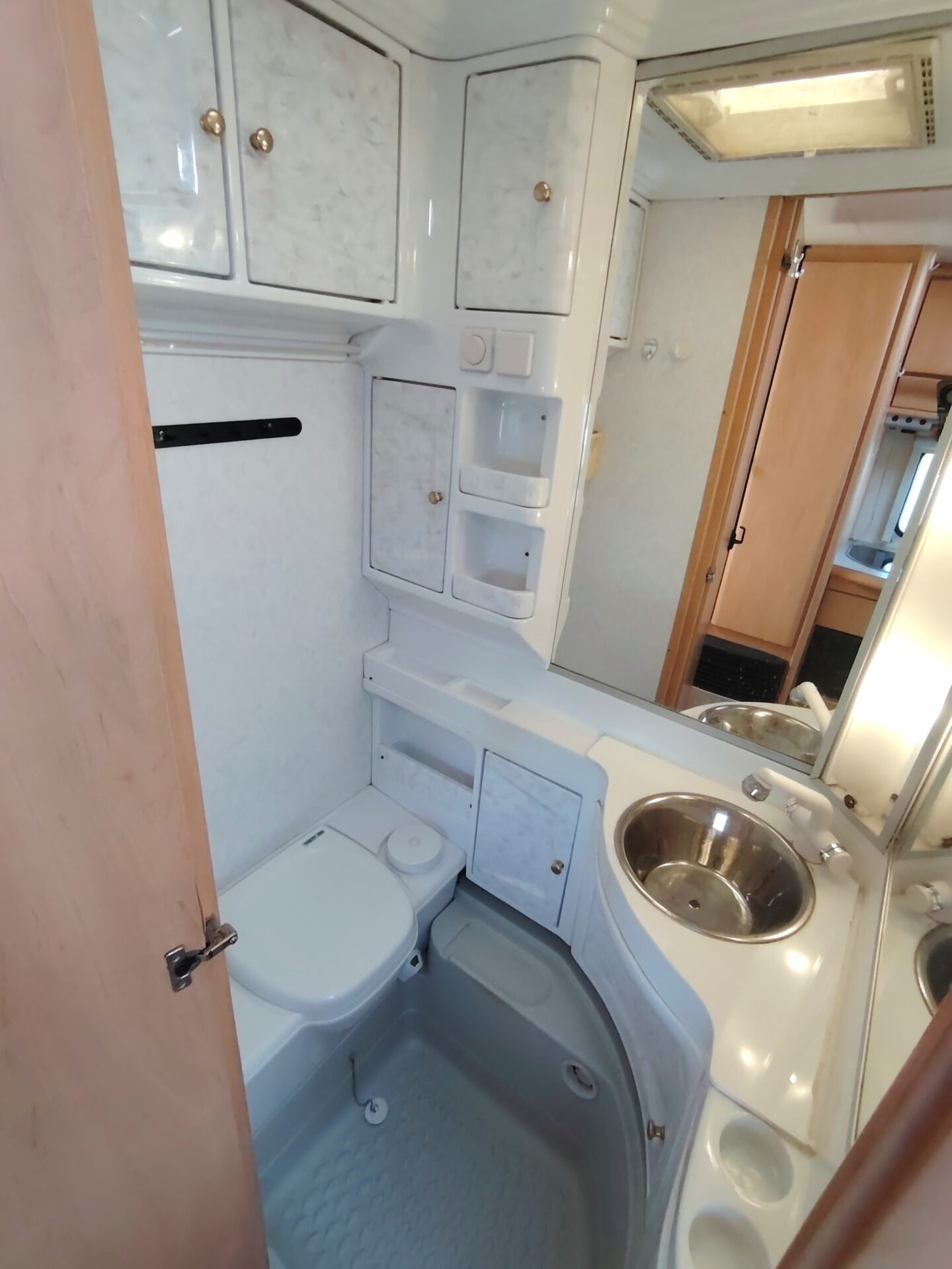 Obrázek interiéru karavanu s koupelnou, toaletou a umyvadlem. Moderní design pro pohodlí na cestách.