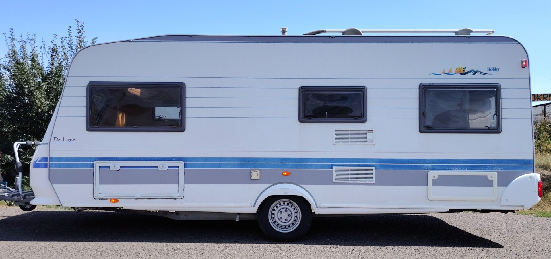 Karavan Hobby De Luxe v bílém provedení, ideální pro pohodlné cestování a rekreaci.