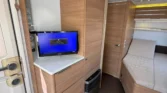 Obrázek interiéru obytného auta s moderním designem, TV a pohodlnými prostory pro spaní. Vybavení z kvalitního materiálu.
