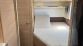 Interiér obytného vozu se světlým dřevěným dekorem a pohodlnou postelí. Ideální pro komfortní cestování.