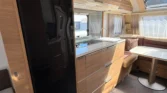 Interiér karavanu s moderní kuchyní a pohodlným posezením, ideální pro cestování a odpočinek.