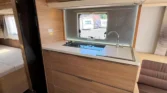 Interiér obytného vozu s moderní kuchyní a pohodlným sezením. Elegantní dřevěné prvky a přirozené osvětlení.