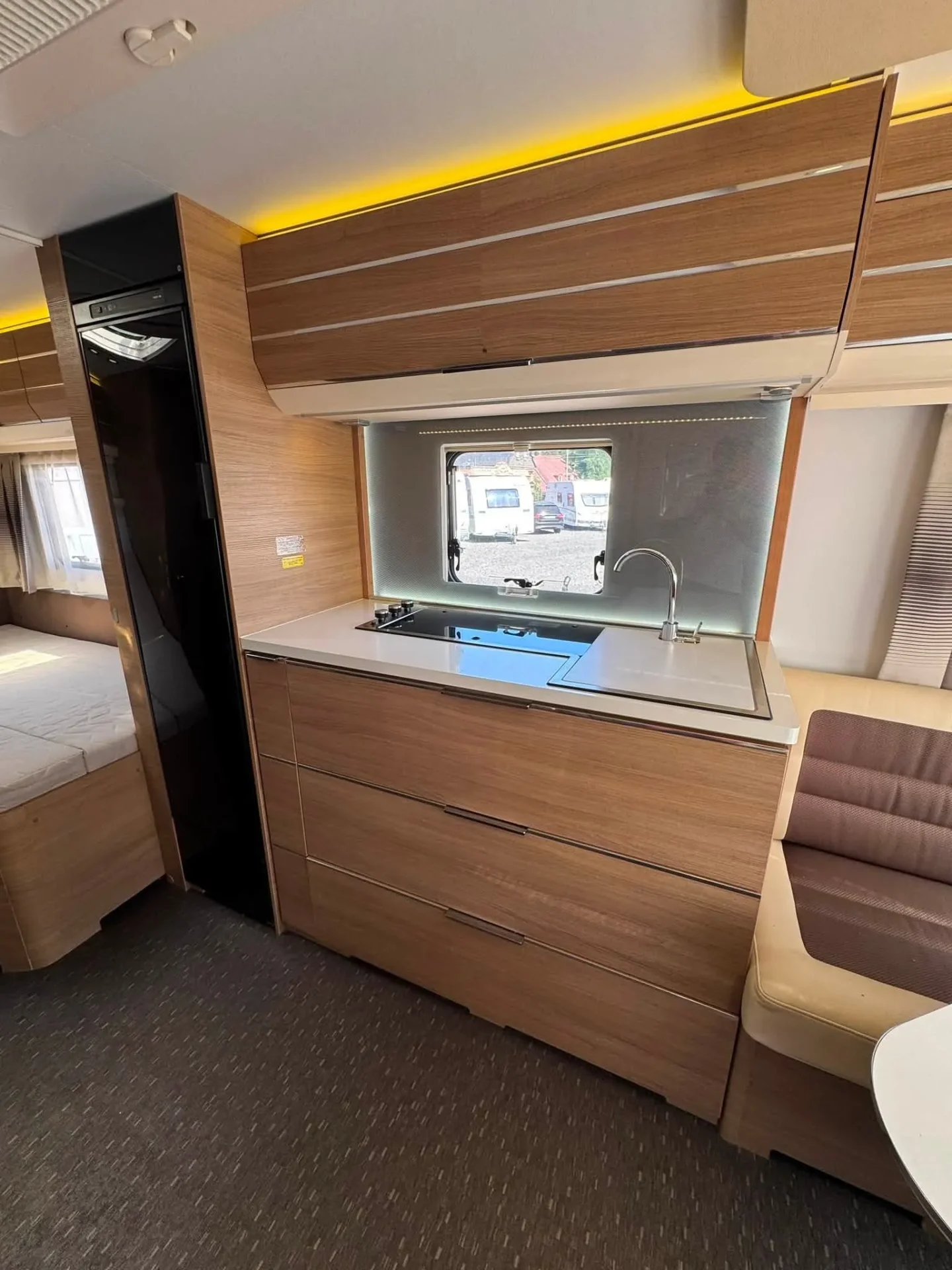 Interiér obytného vozu s moderní kuchyní a pohodlným sezením. Elegantní dřevěné prvky a přirozené osvětlení.