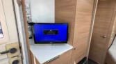 Obrázek interiéru obytného auta s dřevěným nábytkem a televizorem. K dispozici je pohodlné a moderní vybavení.