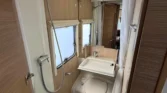 Obrázek interiéru karavanu s moderní koupelnou a sprchovým koutem. Elegantní dřevo a úložné prostory.